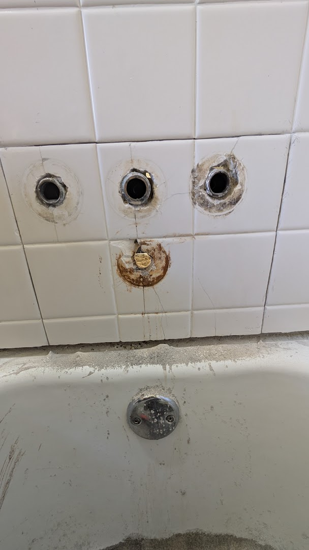 Bathtub wall with removed and damaged shower handle fittings before repair